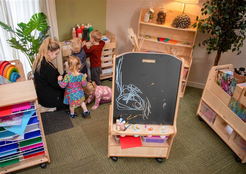 A classroom with a variety of arts and crafts furniture, with a group of children and teacher engaging with it.